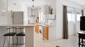 A compact kitchen with a washing machine, a microwave, and a bar counter with two stools. - Holiday Home "Almadraba 2 - Andalmar" close to the Sea with Wi-Fi (Conil)