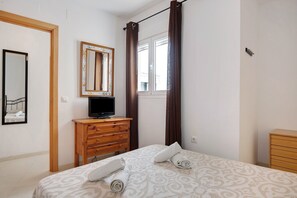 A bedroom with a bed, a wooden dresser, a television, a mirror, and a window with curtains.