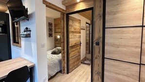 Quarto moderno com parede de madeira, cama com manta estampada, escrivaninha com cadeira e prateleira pequena com objetos decorativos.