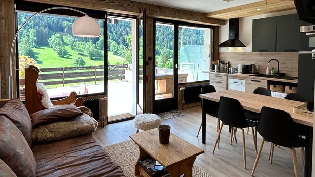 Uma sala de estar moderna com uma janela ampla, um sofá, uma mesa de centro e um espaço de jantar com cadeiras.