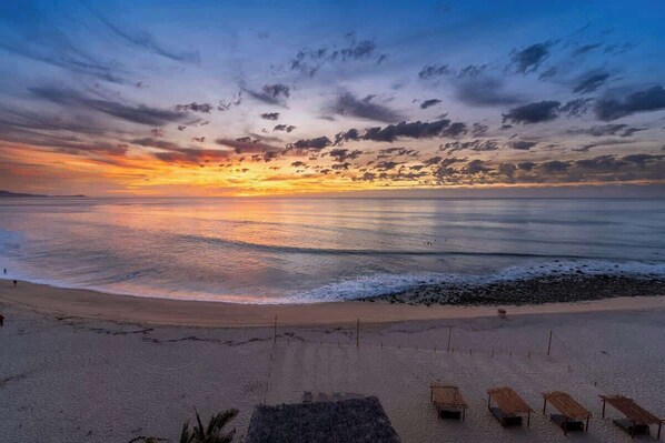 Una playa con un atardecer, mar tranquilo y tumbonas.