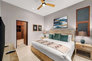 A bedroom with a wooden bed, a ceiling fan, a painting, and a nightstand with a lamp.