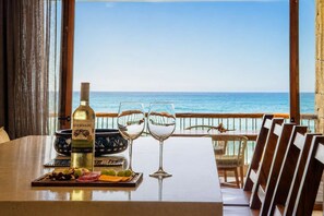 A table with a bottle of wine, two glasses, and a fruit platter, overlooking the ocean.
