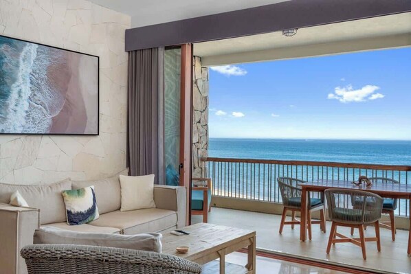 A balcony with a view of the ocean, a sofa, a table, and chairs.