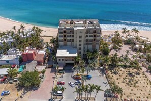 A multi-story hotel with a central courtyard, surrounded by palm trees and a beach view.