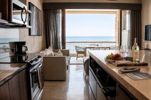 A modern kitchen with a view of the sea, a dining area with a table and chairs, and a bar area with a bottle of wine. - Beautiful Condo at Costa Azul Beach Oceanfront 321 (San José del Cabo)