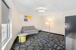 A modern room with a gray sofa, a small round table, a patterned carpet, a ceiling light, and a wall-mounted air conditioner. - Comfort Inn (Kansas City)