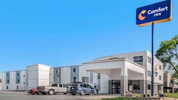 A Comfort Inn hotel with a modern design, a parking lot with several vehicles, and a clear blue sky.