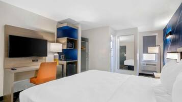 A hotel room with a bed, a TV, a desk with a chair, a wardrobe, and a bathroom visible through an open door.