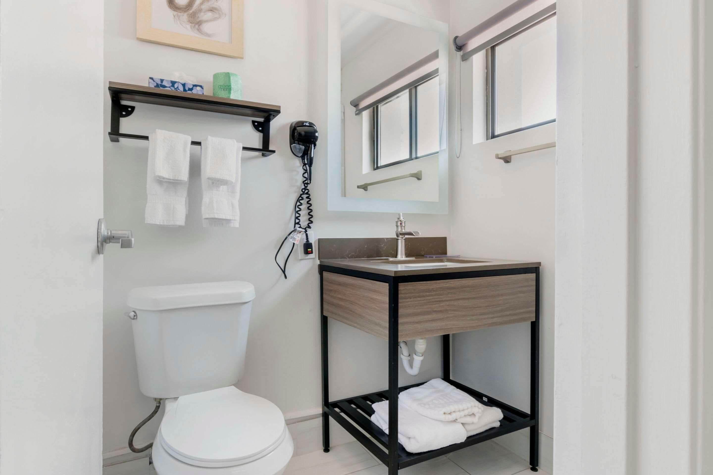 Un bany modern amb vàter, un lavabo amb mirall i una estant amb tovalloles i productes de higiene personal.