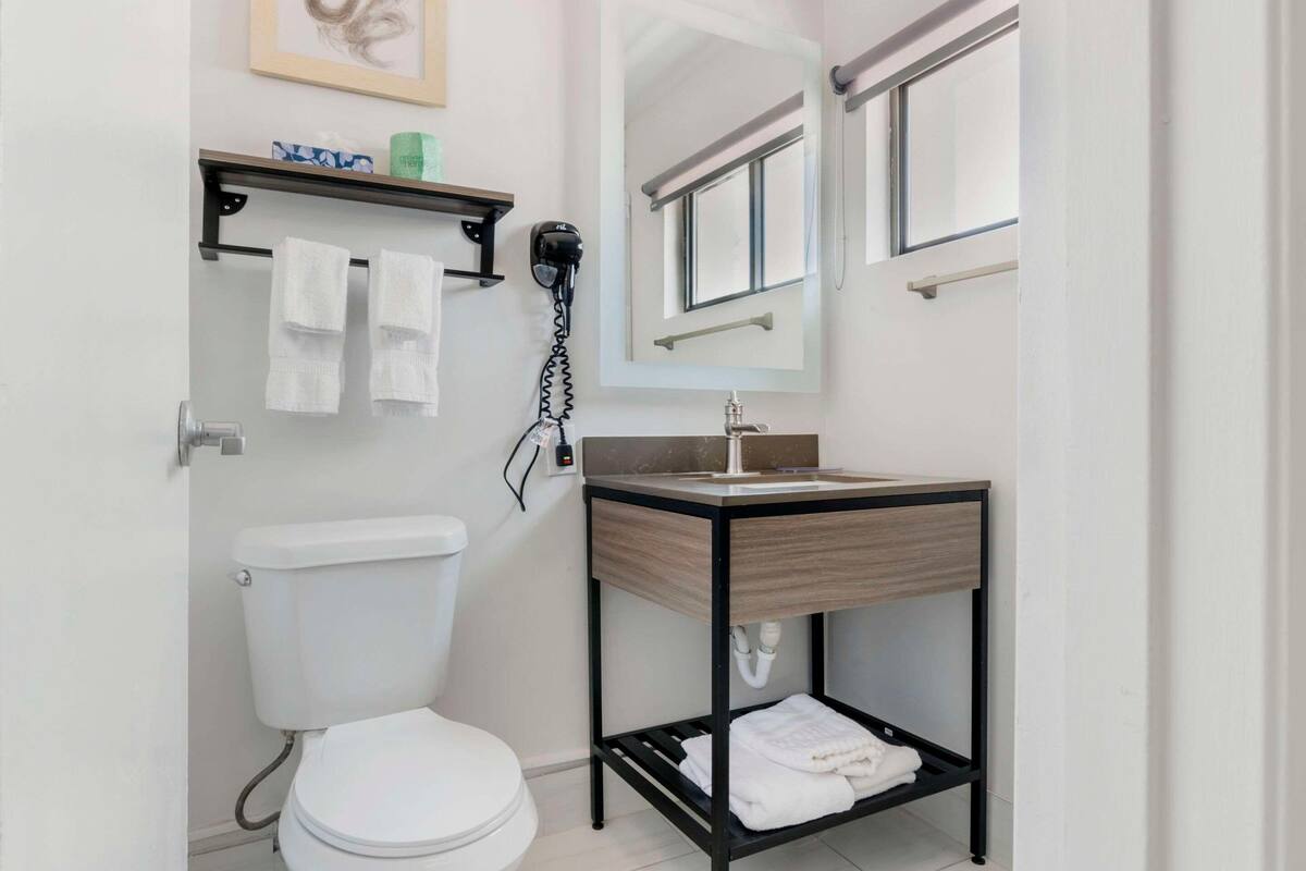 Un baño moderno con inodoro, lavamanos con espejo y repisa con toallas y artículos de aseo.