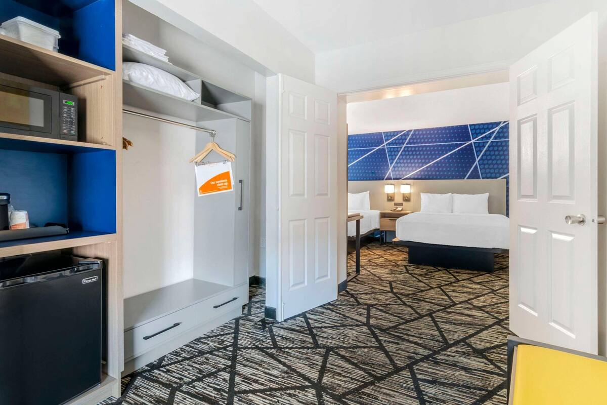 Una habitación de hotel con cama, mesita de noche, lámpara y alfombra estampada.
