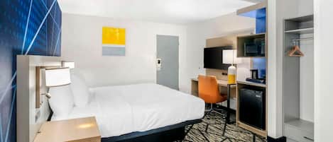 A hotel room with a bed, desk, chair, TV, and a microwave.