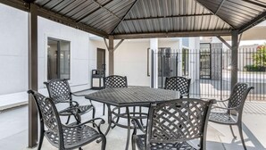 A covered outdoor seating area with a table and chairs, a trash bin, and a building entrance. - Comfort Inn (Kansas City)