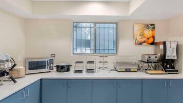 A kitchenette with a microwave, toaster, coffee maker, and a window with blinds.