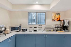 A kitchenette with a microwave, toaster, coffee maker, and a window with blinds. - Comfort Inn (Kansas City)