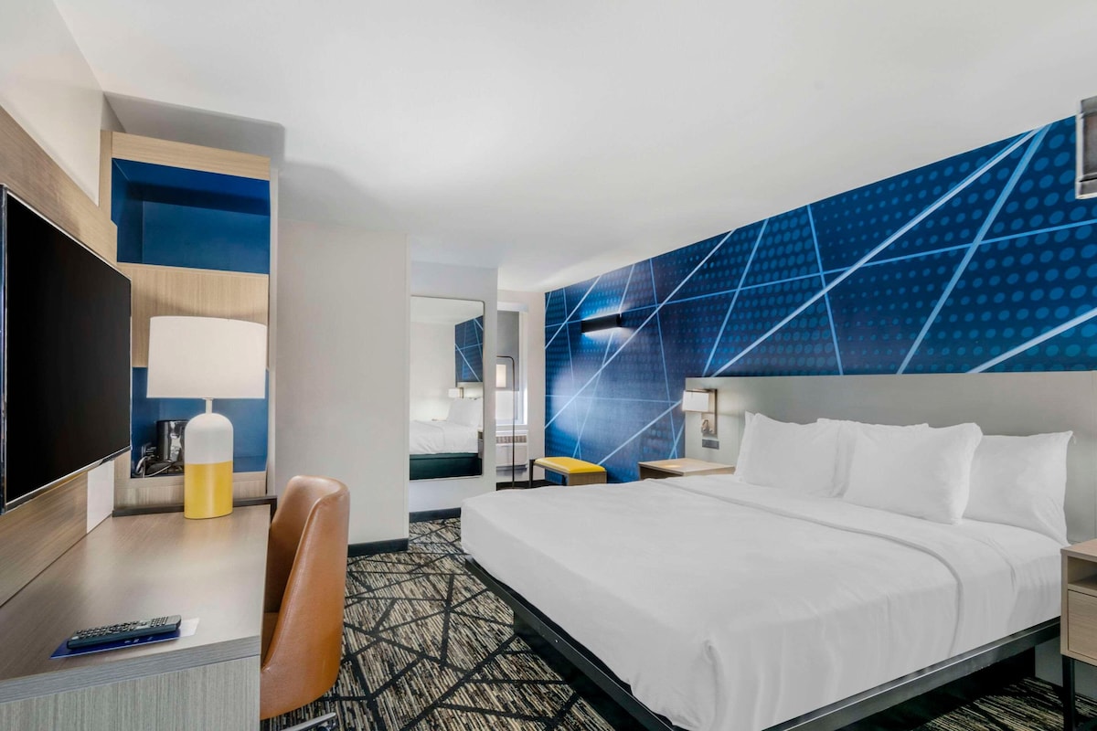 A hotel room with a bed, a desk with a lamp, a TV, and a modern blue wall design.
