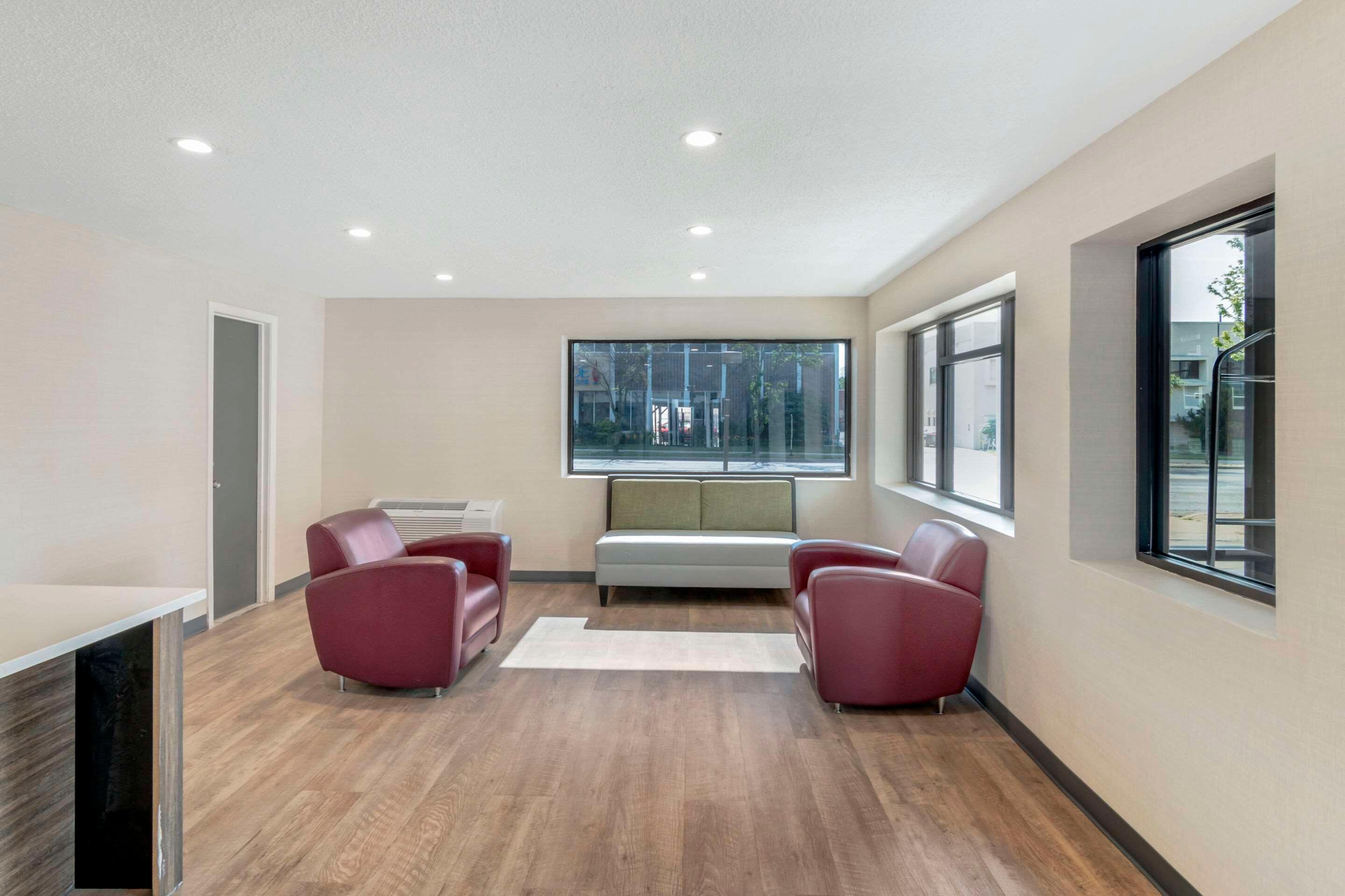 A modern room with a wooden floor, a white sofa, two red chairs, a white table, and a large window.