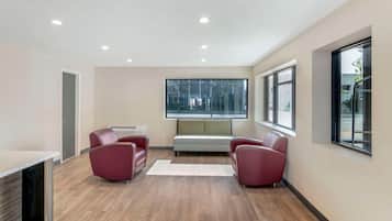 A modern room with a wooden floor, a white sofa, two red chairs, a white table, and a large window.