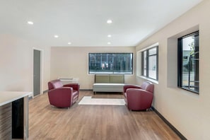 A modern room with a wooden floor, a white sofa, two red chairs, a white table, and a large window.