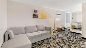 A modern hotel room with a grey sofa, a patterned carpet, and artwork on the wall. - Comfort Inn (Kansas City)