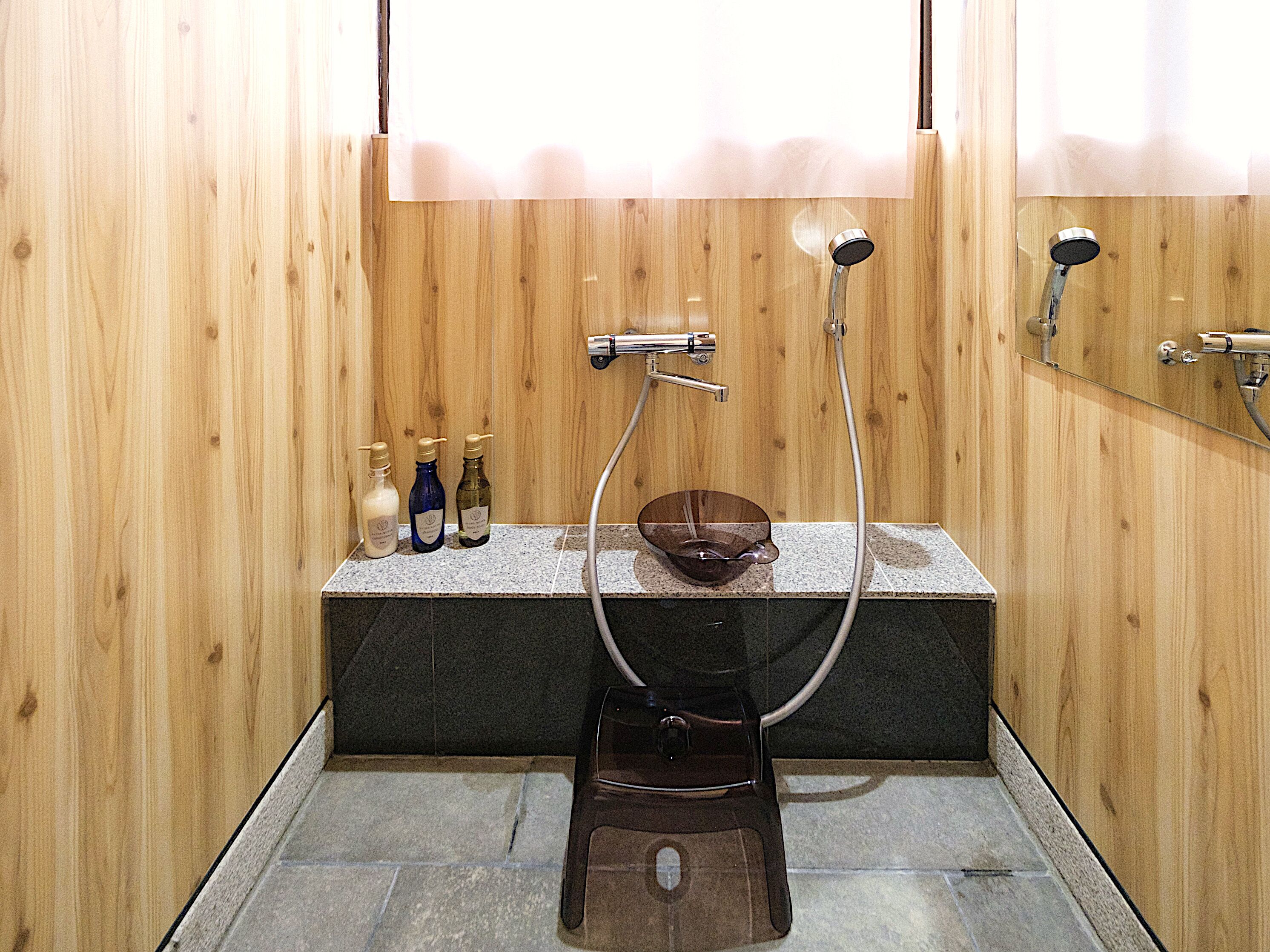 A wooden-paneled bathroom with a stone sink, a handheld showerhead, and three bottles on the counter.