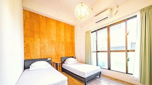 Ein Hotelzimmer mit zwei Betten, einer Wand mit Holzvertäfelung, einem großen Fenster mit Vorhängen und einer Klimaanlage.