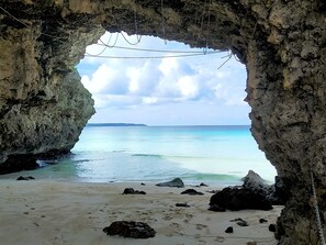 A beach view through a rocky cave entrance with clear turquoise water and a distant landmass. - Guesthouse Re-Spect - Hostel (Miyakojima)