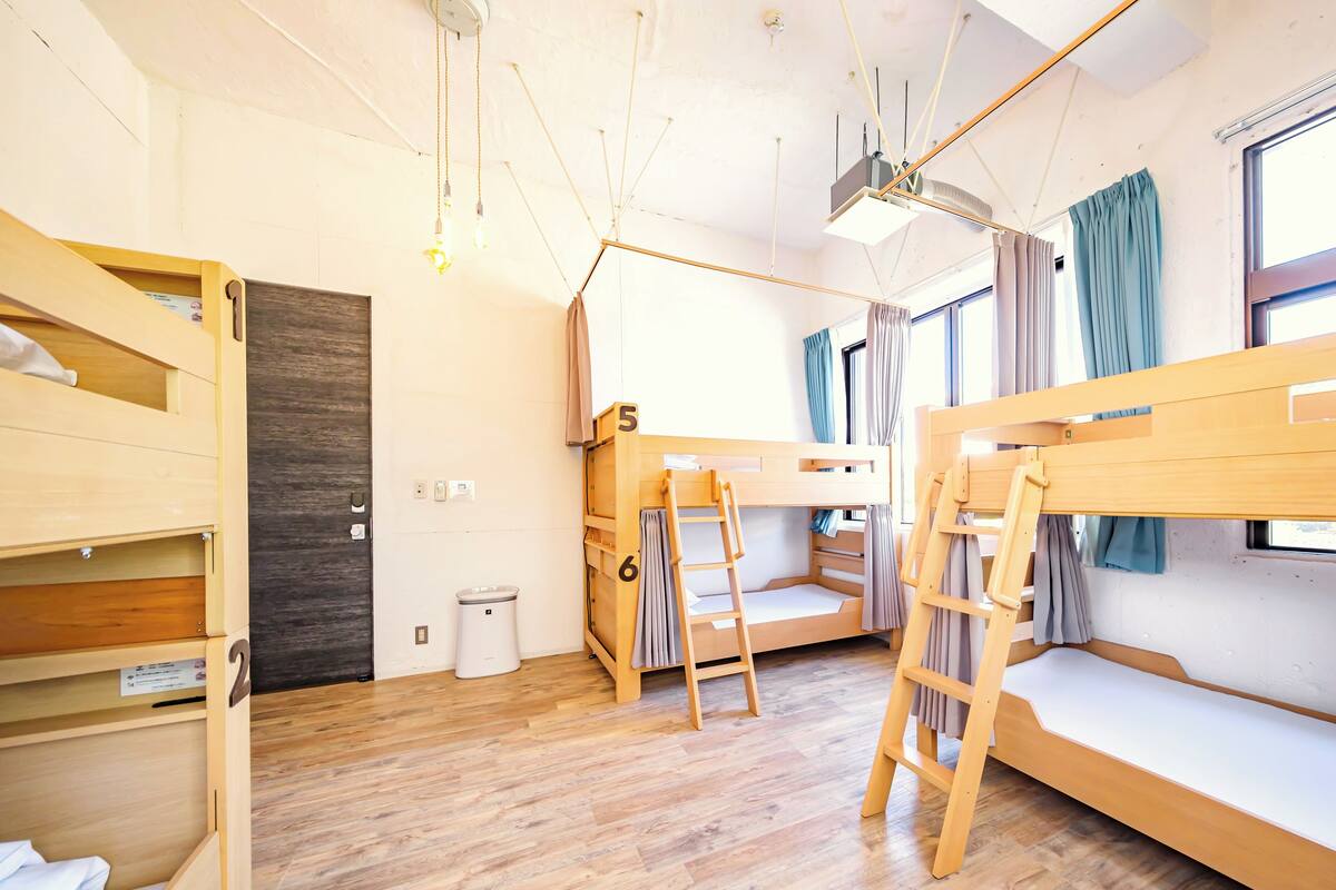 A room with bunk beds, a wooden floor, a ceiling light fixture, and a window with curtains.