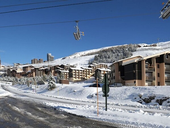 Un centro de esquí cubierto de nieve con varios edificios, incluyendo un hotel grande con balcones y un telesilla en funcionamiento.