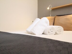 A neatly made bed with rolled white towels, a grey textured blanket, and a wooden headboard.