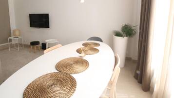 Een moderne eetruimte met een witte tafel, geweven placematen, hangende吊灯 en een pot met een plant.
