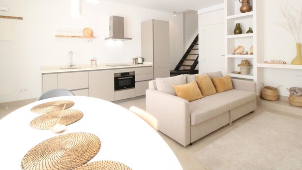 A modern kitchen with white cabinets, a built-in oven, and a dining area with a white table and woven placemats. - Modern Duplex Apartment Near Beach & Center - Del Parque Flats Constancia V3 (Málaga)