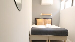 A small, neatly arranged bedroom with a bed, bedside table, and a wall-mounted air conditioner. - Modern Duplex Apartment Near Beach & Center - Del Parque Flats Constancia V3 (Málaga)