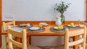 A wooden dining table set with plates, cutlery, a pitcher, and a vase with green leaves. - Charming Village House with Terrace, Near Beach, WiFi, Garage & Fully Equipped Kitchen (Palamós)