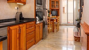 A modern kitchen with wooden cabinets, stainless steel appliances, and a marble floor. - Charming Village House with Terrace, Near Beach, WiFi, Garage & Fully Equipped Kitchen (Palamós)