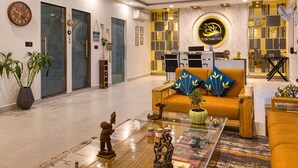 A modern hotel lobby with a reception desk, a sofa with decorative pillows, a coffee table with figurines, and a clock on the wall. - Pumpkin Hotels Corbett, Tusk N Wood (Ramnagar)