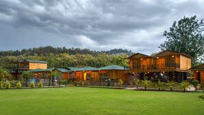 A wooden lodge with multiple cabins, a large lawn, and a forested backdrop. - Pumpkin Hotels Corbett, Tusk N Wood (Ramnagar)