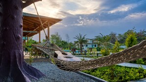 A hammock tied to a tree, a wooden structure, and a pool area with a view of houses and greenery. - Pumpkin Hotels Corbett, Tusk N Wood (Ramnagar)