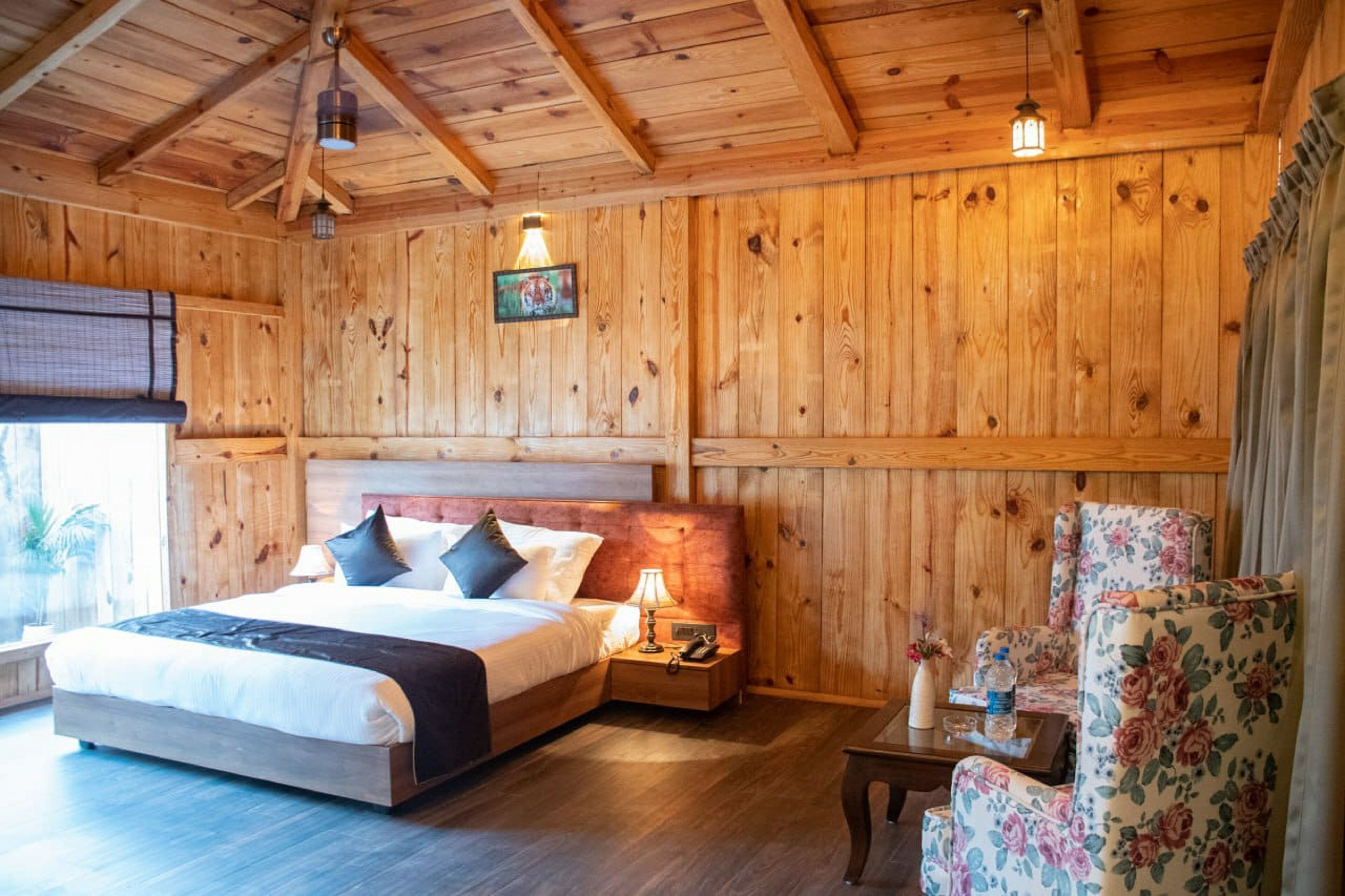 A wooden-paneled room with a bed, nightstands, a chair, and a hanging light fixture.