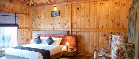 A wooden-paneled room with a bed, nightstands, a chair, and a hanging light fixture.