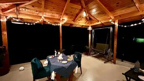 An outdoor wooden pavilion with a table set for dining, string lights, and a swing chair. - Pumpkin Hotels Corbett, Tusk N Wood (Ramnagar)
