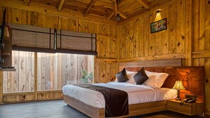 A wooden room with a bed, nightstand, and a window with blinds. - Pumpkin Hotels Corbett, Tusk N Wood (Ramnagar)