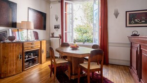 A dining area with a wooden table and chairs, a cabinet with glass doors, and a window with curtains. - Style Bohème, by Veeve (Paris)