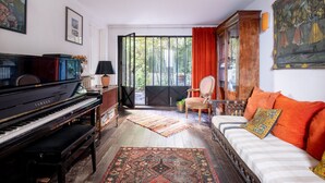 A living room with a piano, a sofa, a chair, and a large window with curtains. - Style Bohème, by Veeve (Paris)