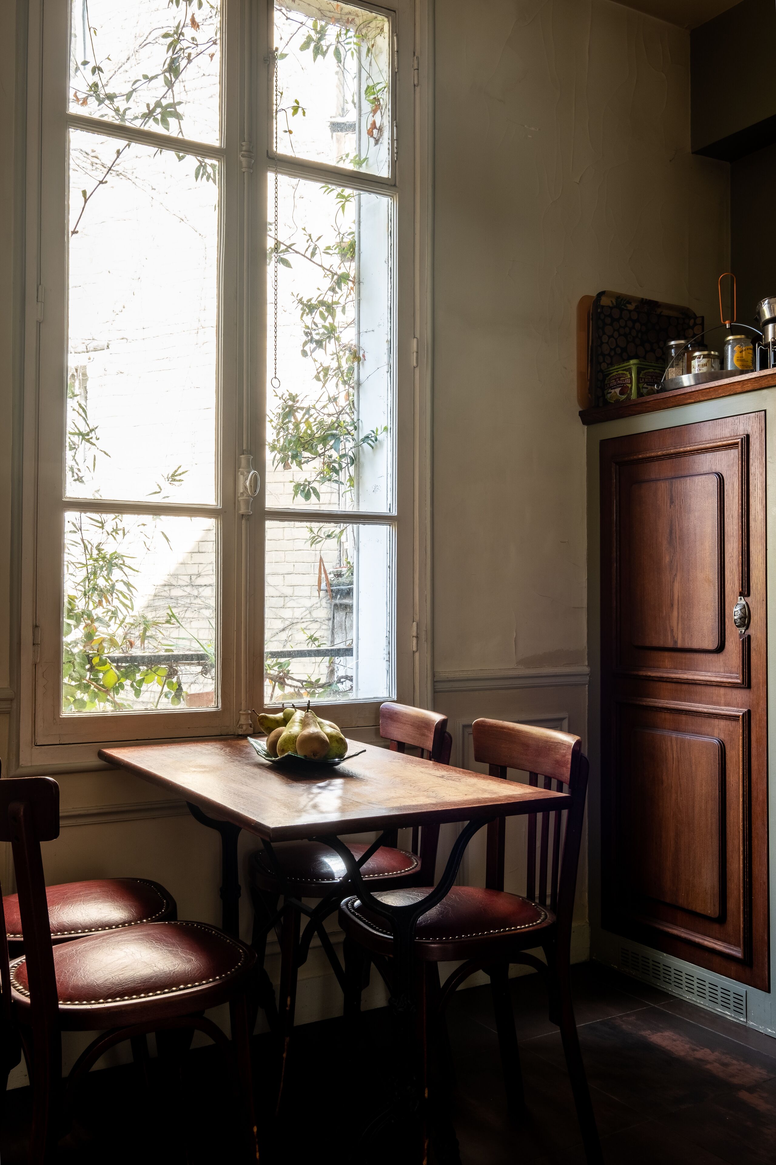 Un comedor con mesa y sillas de madera, una ventana que da a zonas verdes y un mueble de madera.