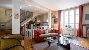 A spacious living room with a glass coffee table, a sofa, and a staircase leading to an upper floor. - Style Bohème, by Veeve (Paris)