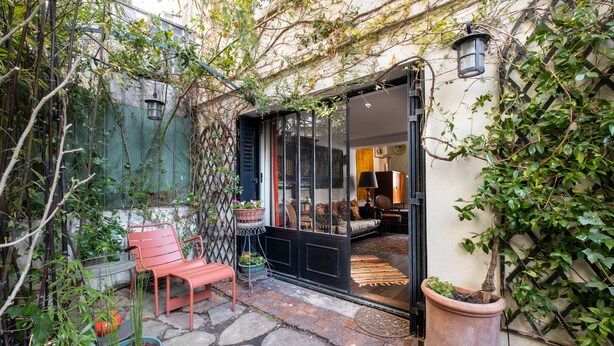 A cozy outdoor seating area with a bench and potted plants, a glass door entrance, and a small patio with a rug. - Style Bohème, by Veeve (Paris)