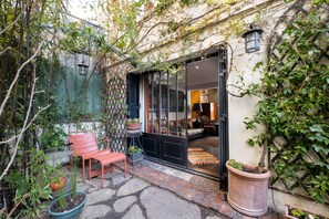 A cozy outdoor seating area with a bench and potted plants, a glass door entrance, and a small patio with a rug. - Style Bohème, by Veeve (Paris)