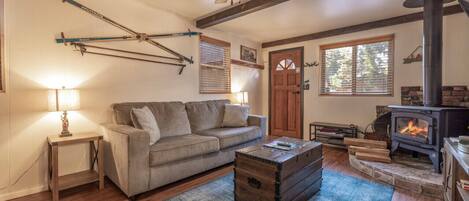 A cozy living room with a sofa, a wooden coffee table, a fireplace, and skis mounted on the wall.